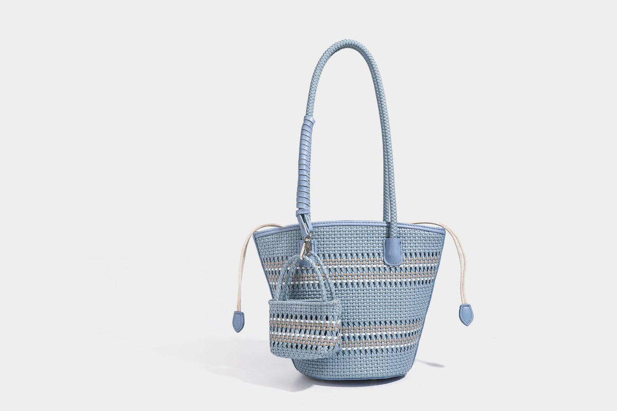 Light blue open-weave woven bucket tote bag with long braided shoulder straps, drawstring side ties, and attached mini pouch