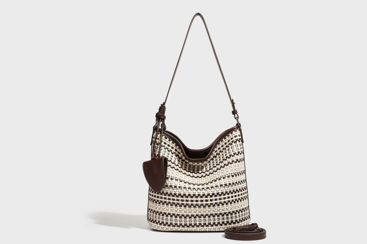 Woven stripe bucket shoulder bag in cream and dark brown with leather-look trim, knotted adjustable strap, and small shield