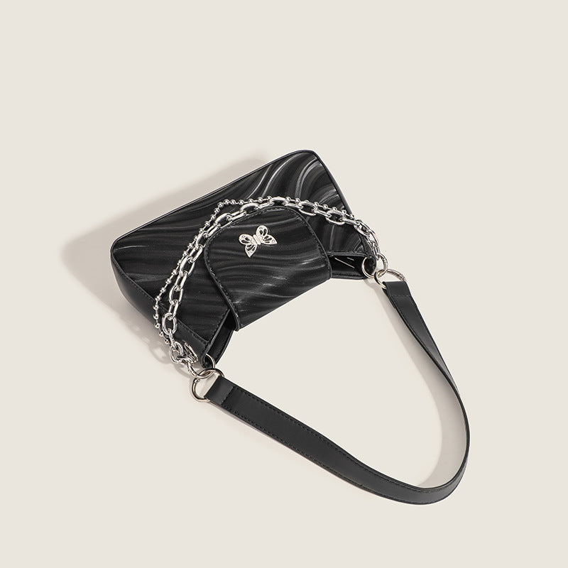 Small trapezoid shoulder bag with ripple leather-look finish, silver butterfly front clasp, and layered chain-and-ball strap