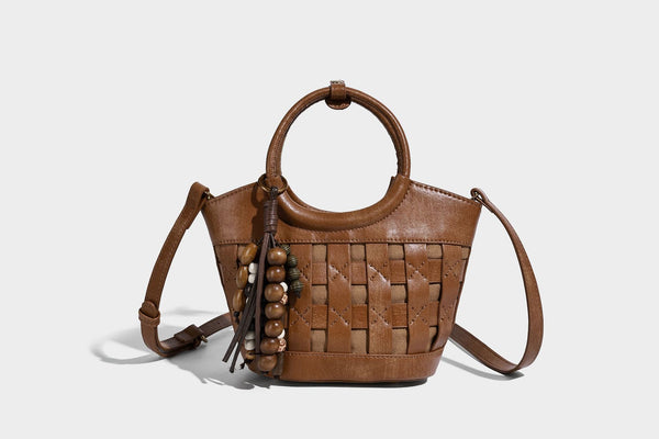 Small woven-panel bucket bag with circular ring handles, beaded tassel charm, and detachable crossbody strap in brown, detail