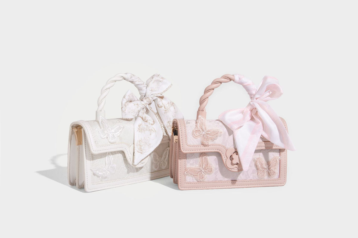 Small structured white flap bag with butterfly embroidery, flower-shaped turn-lock clasp, braided top handle with scarf bow