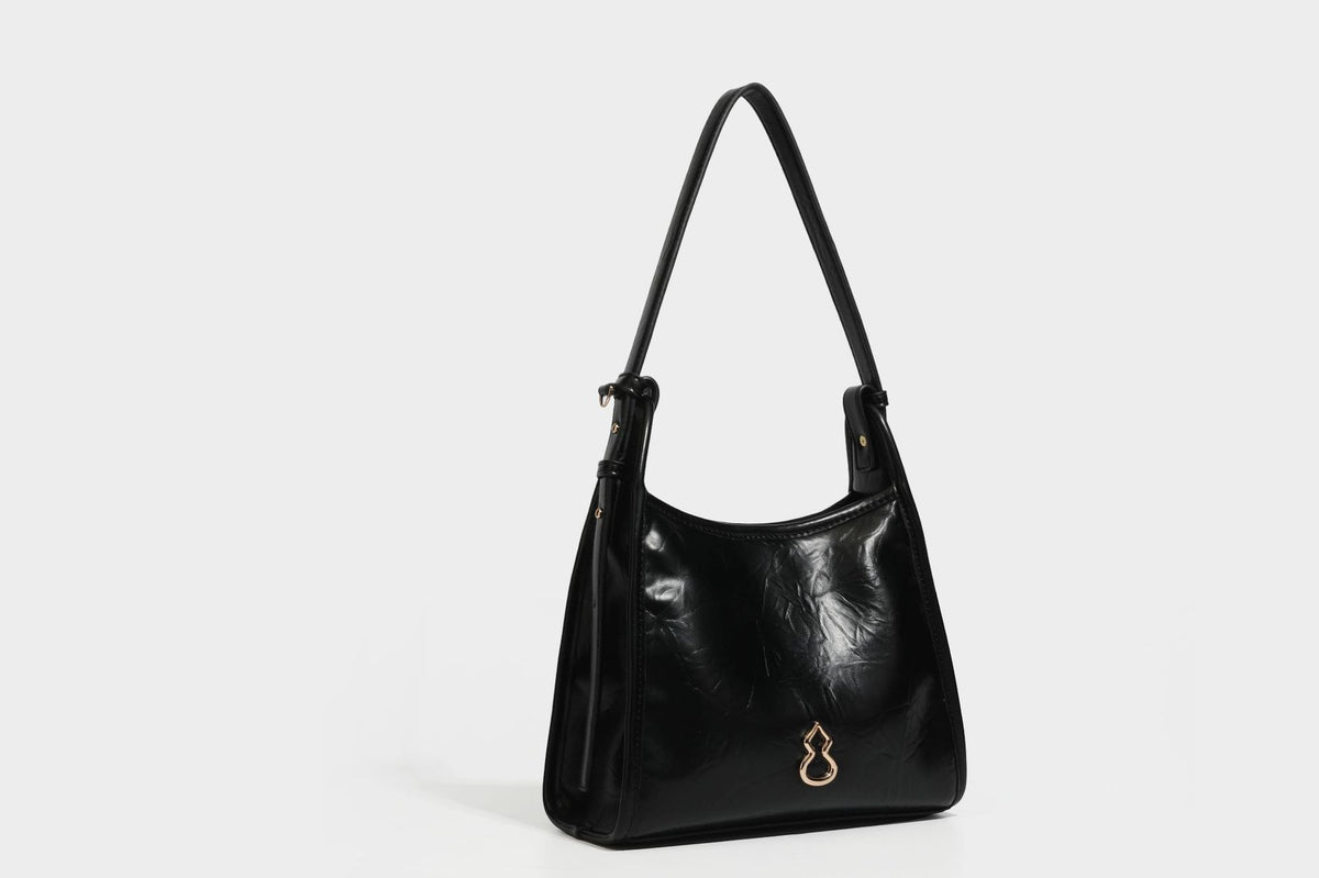 Strukturierte, trapezförmige Schultertasche aus glänzender, geknautscht wirkender Lederoptik mit goldfarbenen Beschlägen auf der Vorderseite und langem, verstellbarem