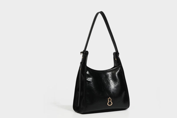 Strukturierte, trapezförmige Schultertasche aus glänzender, geknautscht wirkender Lederoptik mit goldfarbenen Beschlägen auf der Vorderseite und langem, verstellbarem