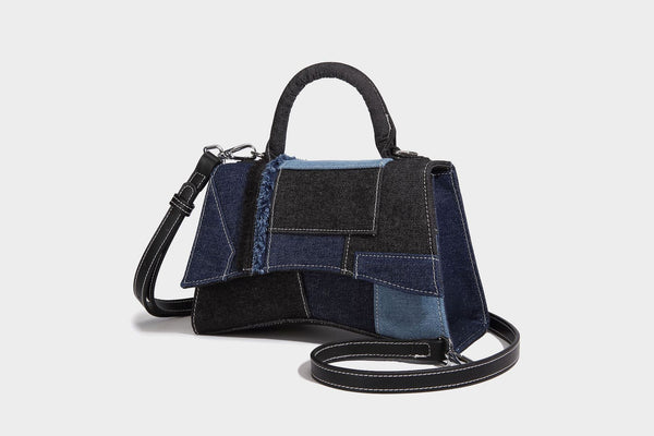 Structured patchwork denim trapezoid satchel bag with frayed panel trim, rounded top handle, and silver-tone hardware, detail