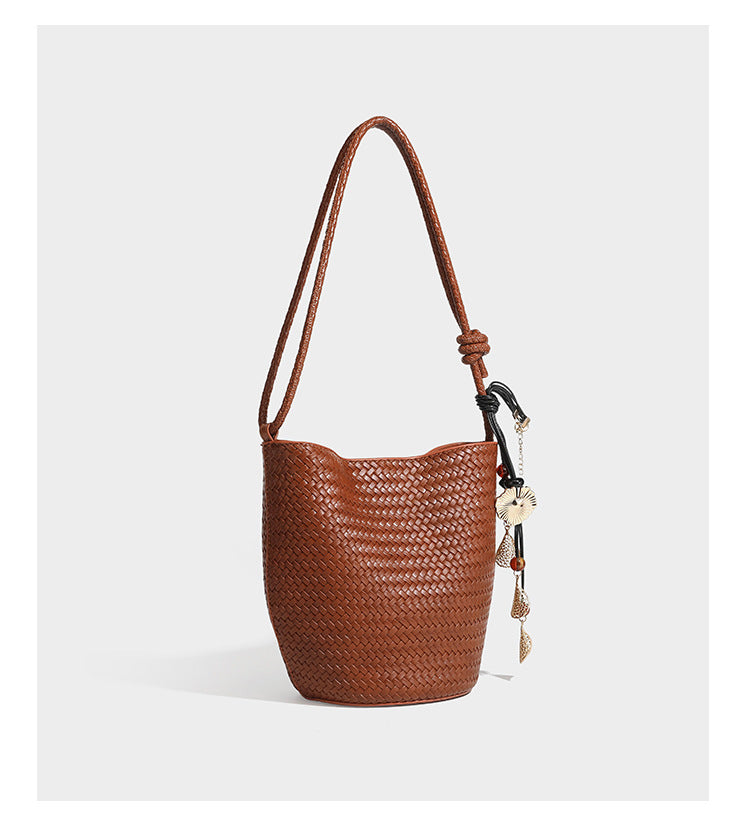 Olive green woven leather-look bucket bag with braided crossbody strap, knotted adjustment, and gold-tone tassel charm with