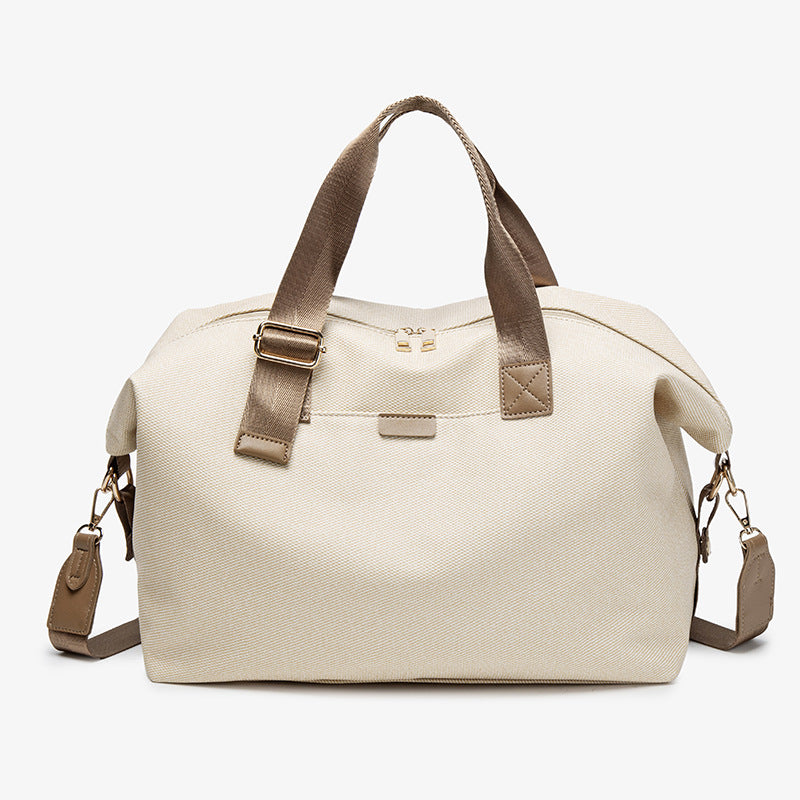 Structured woven duffel bag with dual tan webbing handles, detachable shoulder strap, top zip closure, and gold-tone