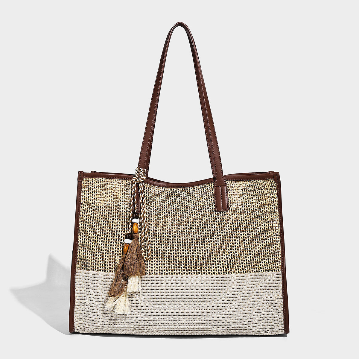 Two-tone woven straw tote bag with leather-look brown trim, long shoulder straps, and knotted tassel charm, detail view 6