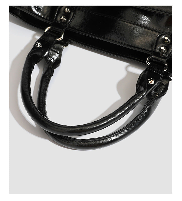 Black glossy structured tote bag with rivet and buckle detail, dual top handles, and detachable shoulder strap, detail view