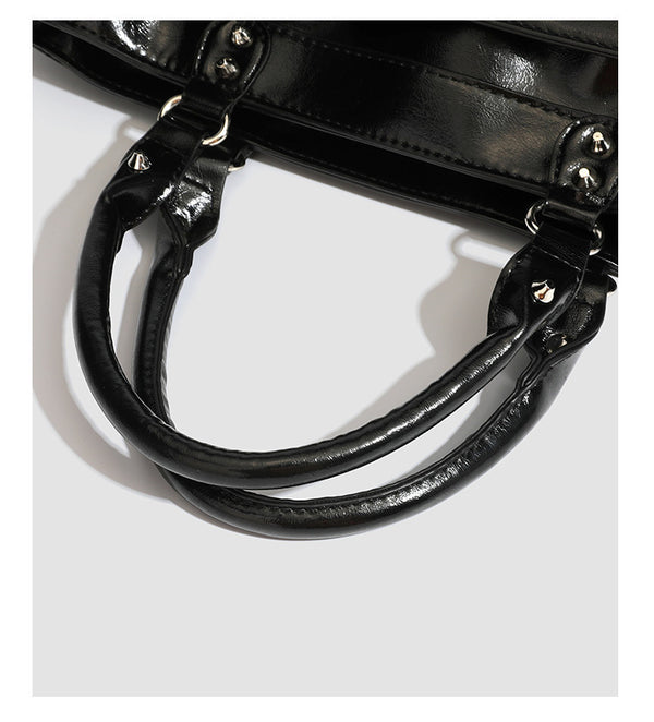 Black glossy structured tote bag with rivet and buckle detail, dual top handles, and detachable shoulder strap, detail view