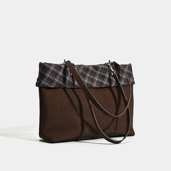 Brown structured tote bag with woven plaid fold-over top panel, silver-tone ring hardware, and long flat shoulder straps