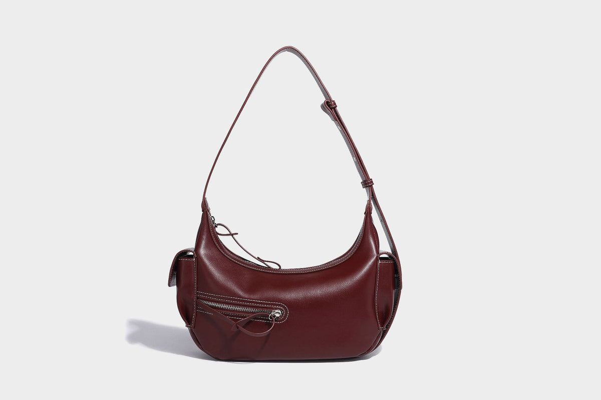 Smooth leather-look crescent shoulder bag with front zip pocket, side flap pockets, adjustable strap, and silver-tone, detail