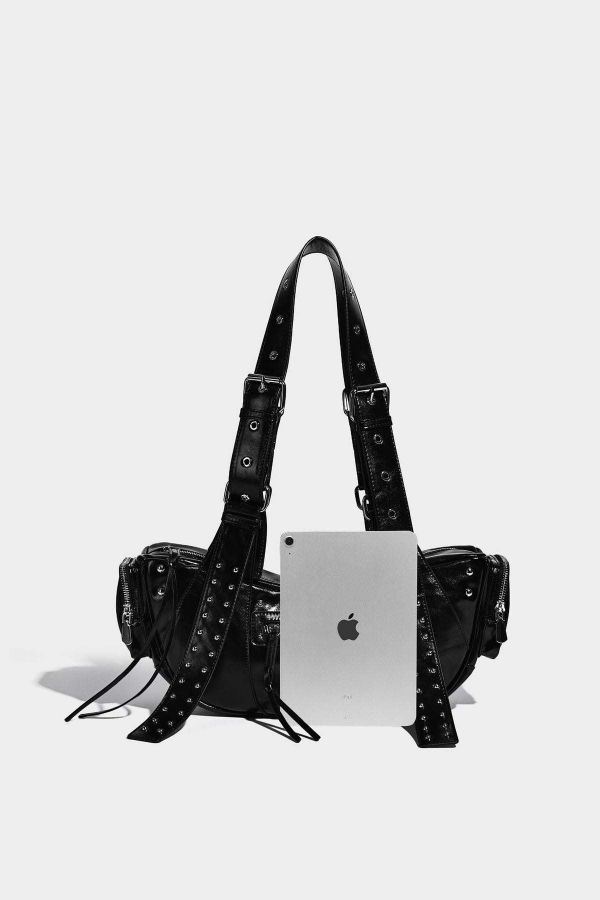 Glossy black crescent shoulder bag with silver-tone rivets, multiple zip pockets, and long adjustable studded straps, detail