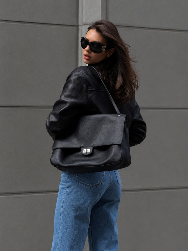 Structured black flap shoulder bag with pebbled texture, silver-tone turn-lock closure, and adjustable single shoulder strap