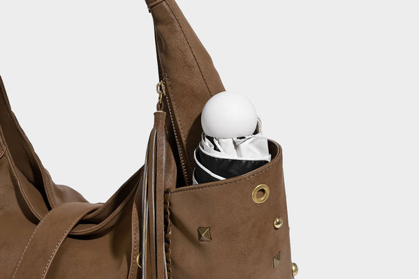 Slouchy crescent hobo bag in matte brown suede-like finish with gold-tone studs, grommets, braided top handle, tassel side