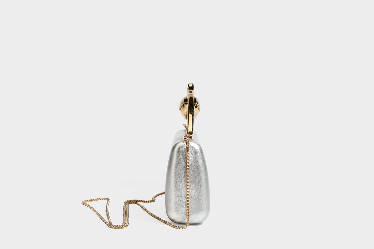 Strukturierte rechteckige Clutch mit goldfarbenem Henkel in Form einer Rosenknospe und abnehmbarem Kettenriemen in Metallic-Optik, Detailansicht