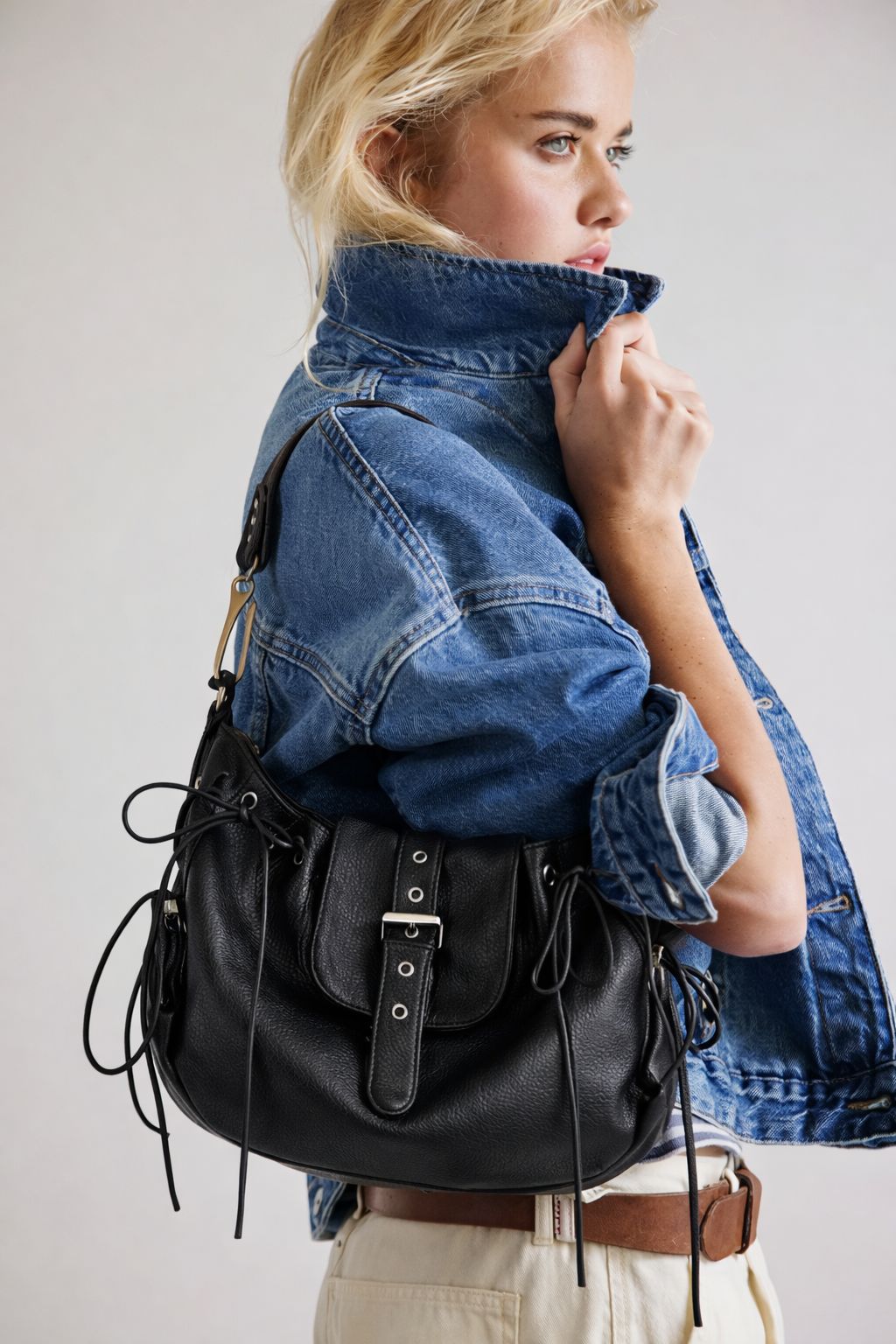 Schwarze Sattelschultertasche in genarbter Lederoptik mit geschnürten Seiteneinsätzen, Ösendetails und Klappe mit silberfarbener Schnalle, Detailansicht