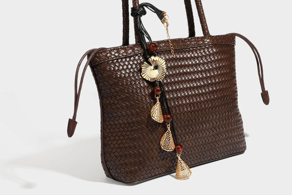 Structured woven leather-look tote bag in dark brown with long shoulder straps, side drawstring ties, and gold filigree