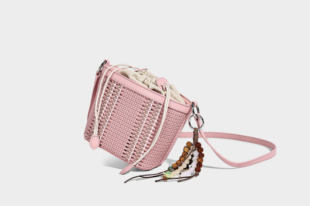 Small woven bucket bag with drawstring top, braided handle, detachable crossbody strap, and silver-tone ring hardware, detail