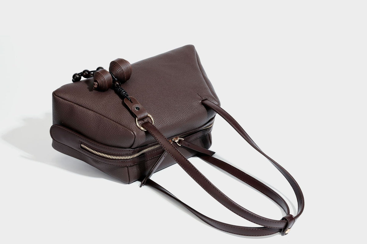 Structured trapezoid shoulder bag in dark brown pebbled leather-look finish with slim double straps, top zip closure, side