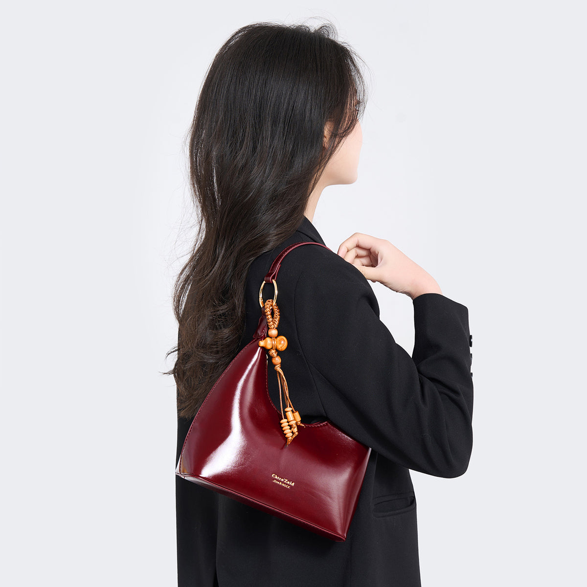 Glossy crescent hobo shoulder bag in deep burgundy with beaded wood tassel charm and gold-tone ring hardware, detail view 3