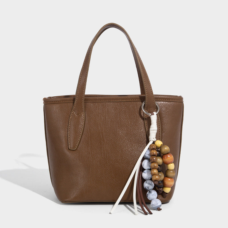 Compact structured bucket tote bag with pebbled textured finish, dual top handles, silver-tone lock hardware, and detachable