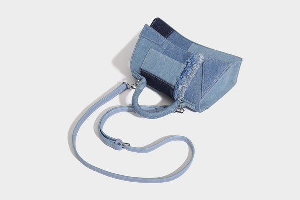 Structured patchwork denim trapezoid satchel bag with frayed panel trim, rounded top handle, and silver-tone hardware, detail