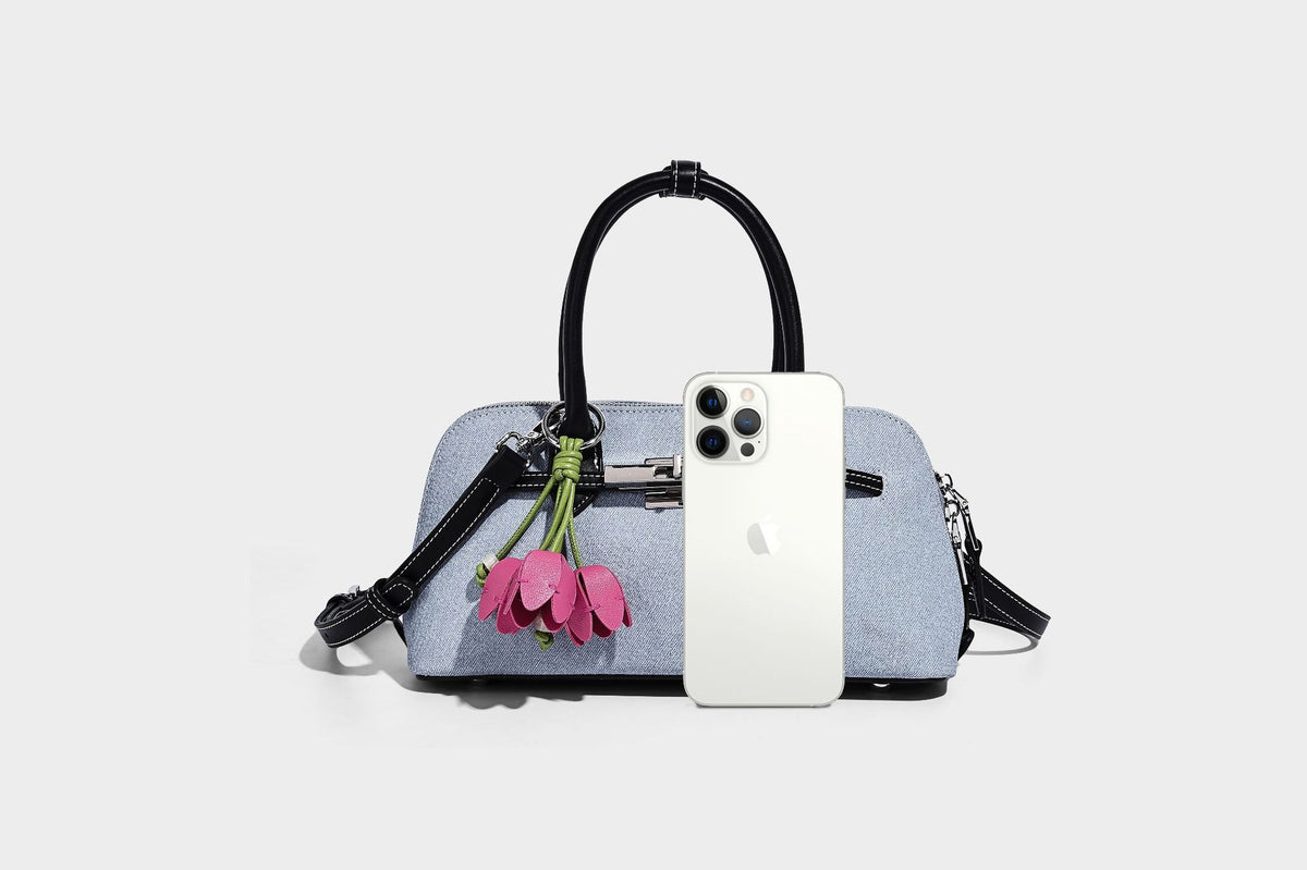 Compact structured satchel in light blue denim-look fabric with black leather-look trim, silver turn-lock closure, rolled