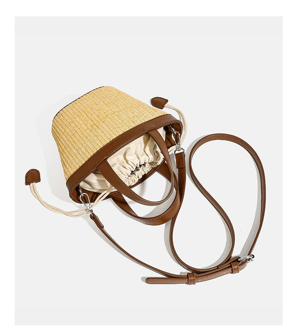 Kleine geflochtene Bucket Bag aus Stroh mit schwarzem Besatz in Lederoptik, zwei oberen Tragegriffen, cremefarbenem Futter mit Kordelzug und seitlichen Kordelverschlüssen