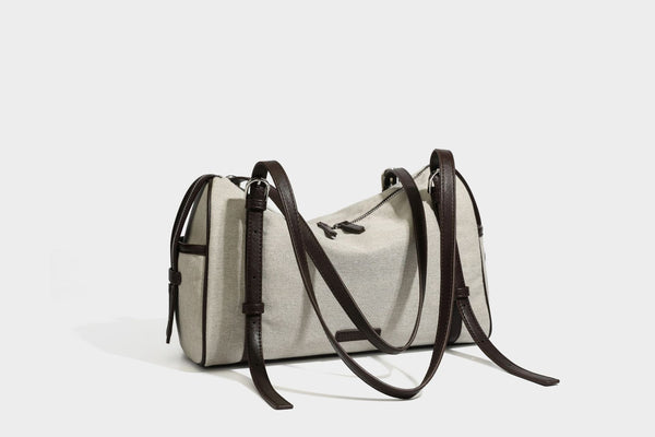 Beige canvas barrel bag with dark brown leather-look trim, silver-tone hardware, top zip closure, and adjustable shoulder