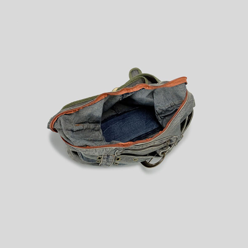 Washed blue-gray denim slouchy hobo shoulder bag with wide grommeted belt panel, brass-tone D-ring buckle, exterior zip