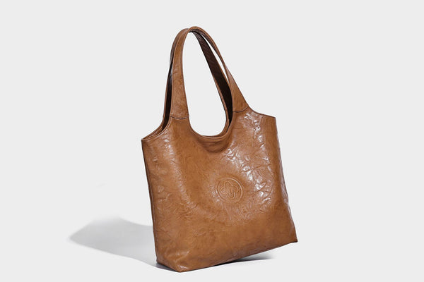 Large open-top tote bag with crinkled leather-look finish, long double shoulder straps, and embossed circular detail on