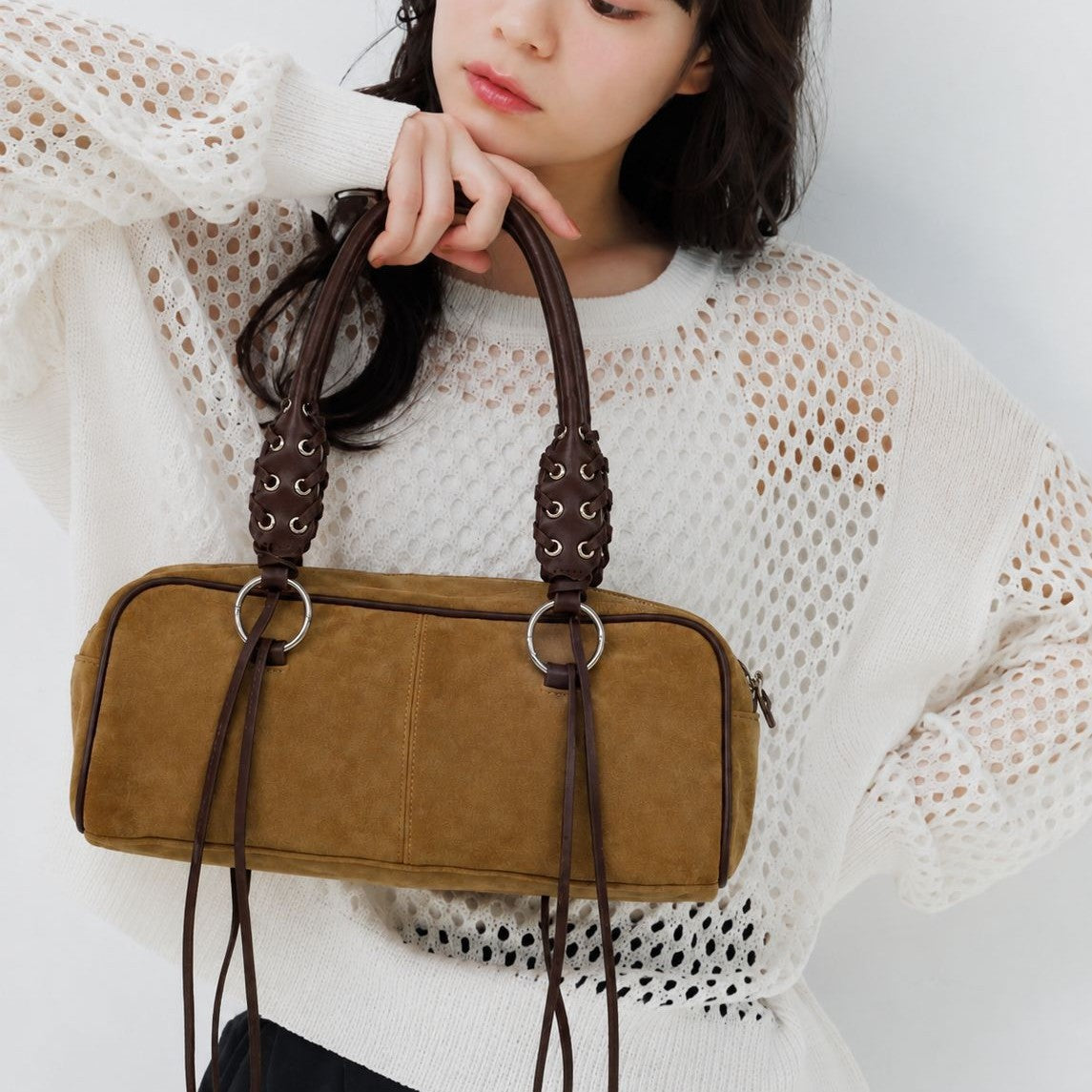 Rectangular suede-look barrel bag with laced eyelet handles, silver O-ring hardware, and hanging leather-look fringe tie