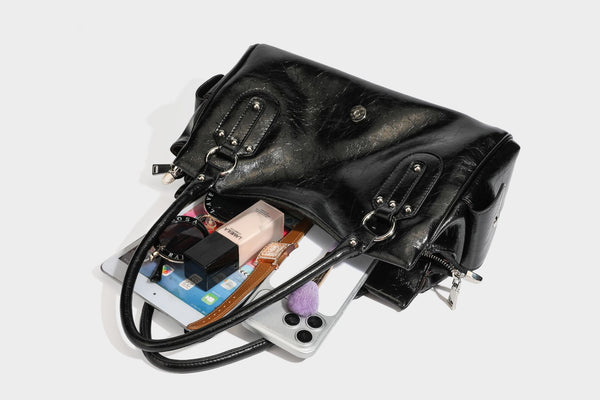 Glänzende, geknautschte Barrel-Satchel mit zwei oberen Tragegriffen, vorderem Klappen-Riemen-Panel, Ring- und Nietenbeschlägen sowie einem abnehmbaren