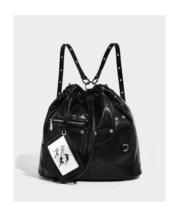 Glossy black convertible bucket backpack with silver grommet-studded straps, drawstring cinch closure, and front zip pocket
