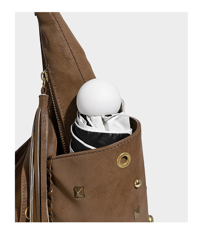 Slouchy crescent hobo bag in matte brown suede-like finish with gold-tone studs, grommets, braided top handle, tassel side