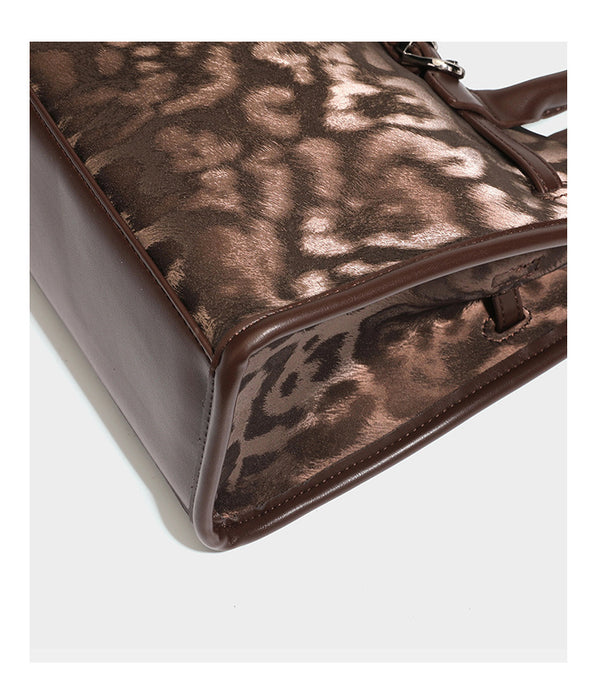 Structured leopard-print tote bag with glossy satin-like finish, dual rounded top handles, silver buckle-and-ring front