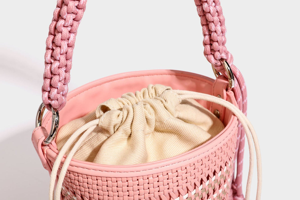 Detailansicht einer zylindrischen, handgeflochtenen Beuteltasche mit geflochtenem Henkel, Kordelzugverschluss, Kordelquasten und Metallringbeschlägen