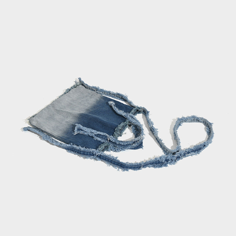 Washed denim fringe crossbody bag with indigo-to-pale-blue gradient and raw fringe trim along edges and shoulder strap