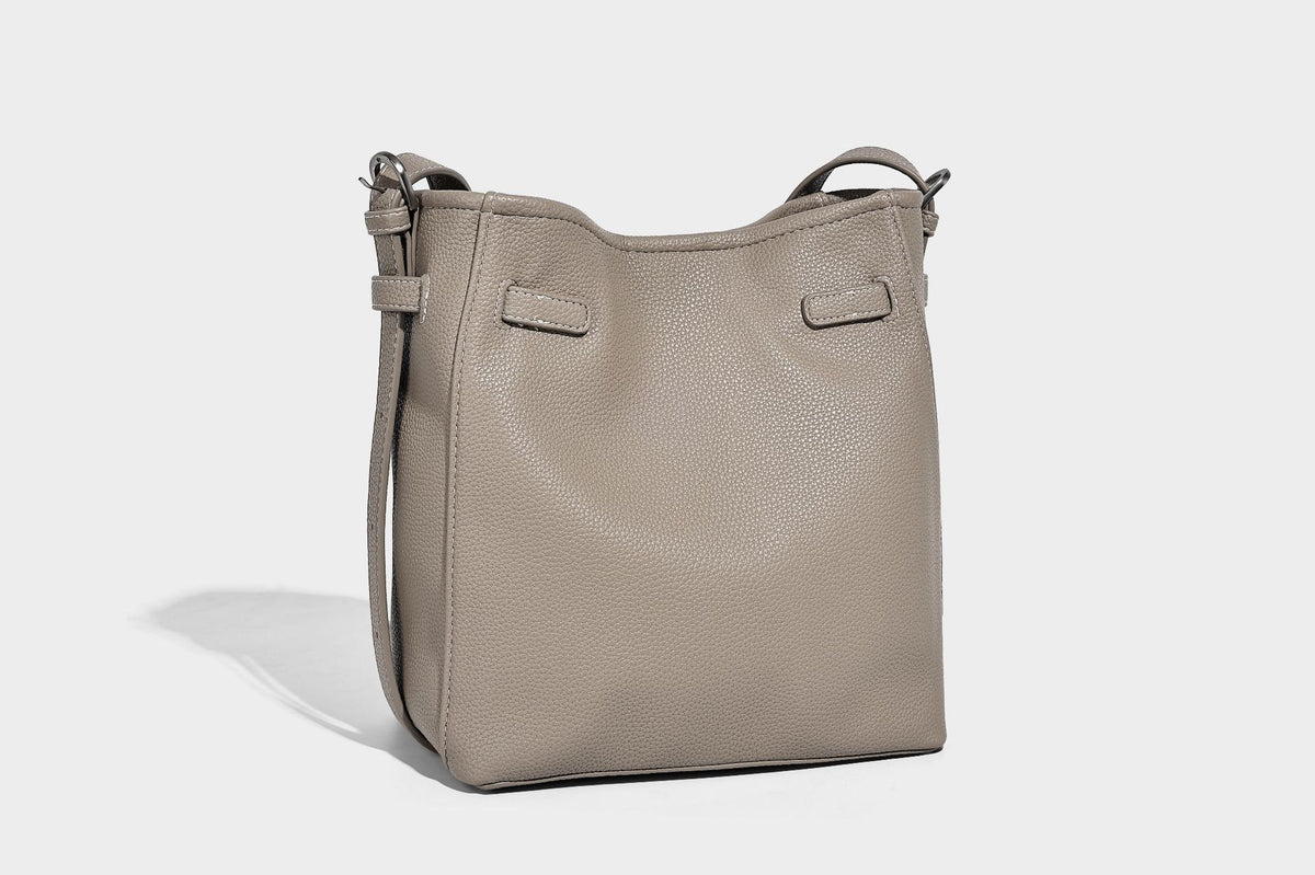 Soft-structured pebbled bucket shoulder bag with front turn-lock strap detail, adjustable strap, and hanging floral tassel
