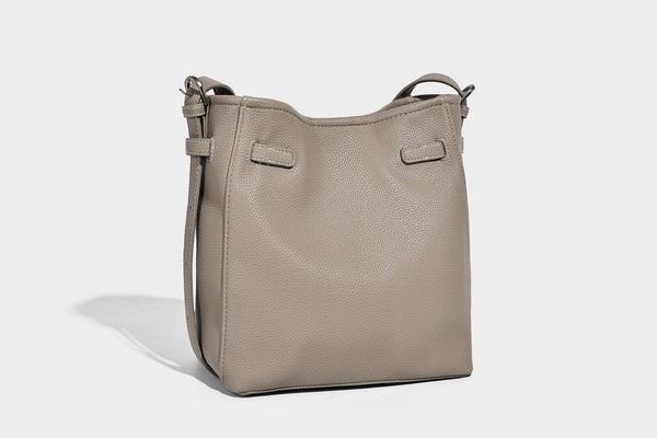 Soft-structured pebbled bucket shoulder bag with front turn-lock strap detail, adjustable strap, and hanging floral tassel