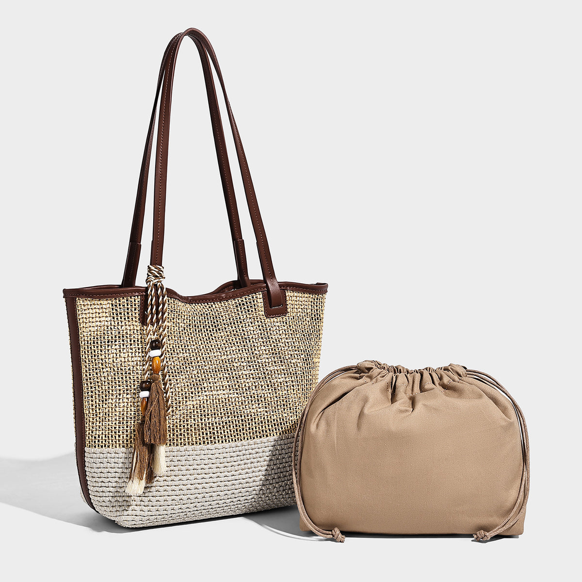 Woven beige and cream tote bag with brown leather-look trim, long double shoulder straps, and knotted tassel charm on front