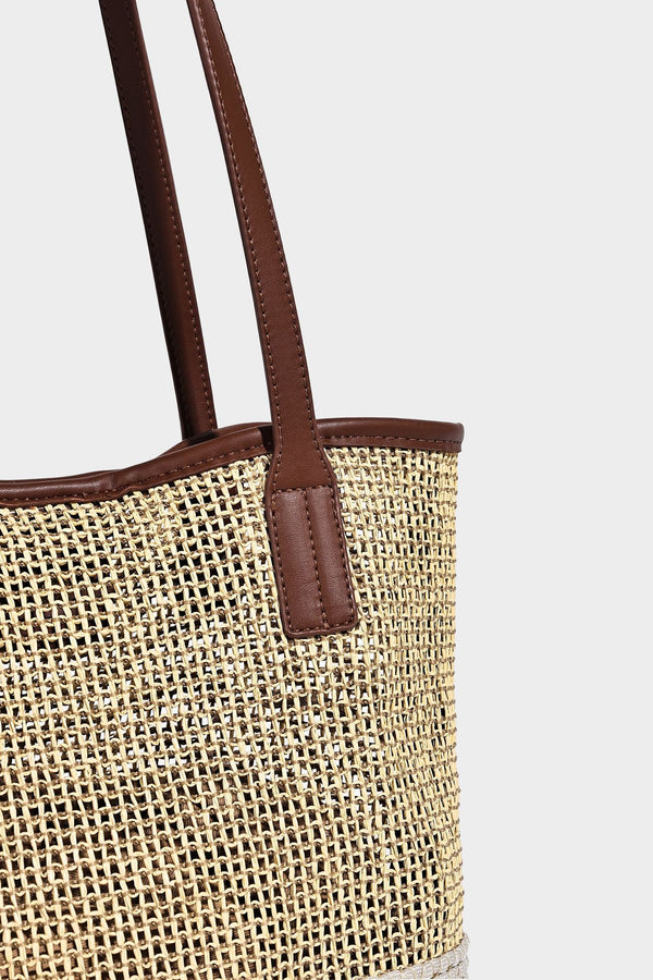 Woven straw-look tote bag in tan and cream with dark brown leather-look trim, long flat shoulder straps, and tassel bead