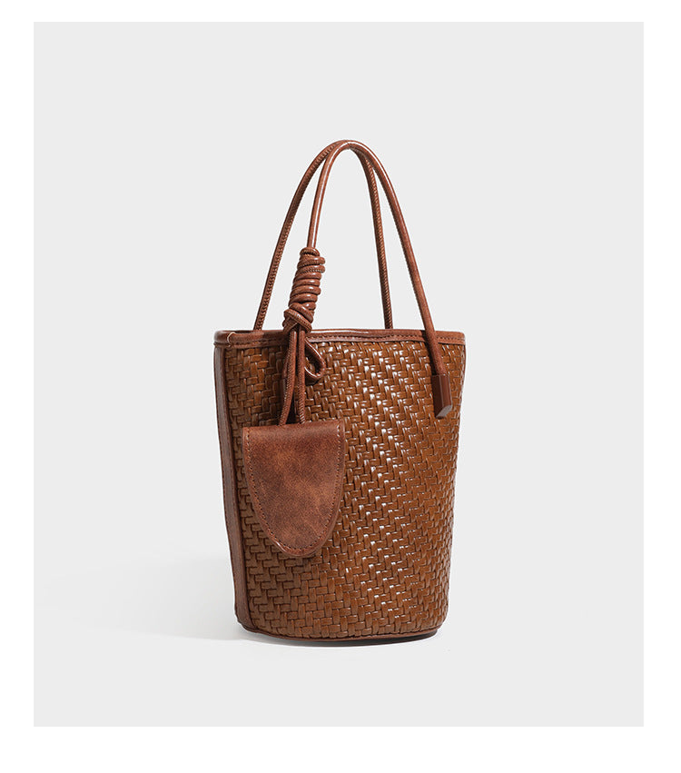 Structured woven-texture leather-look bucket bag in brown with knotted top handles, small front flap pouch, and adjustable