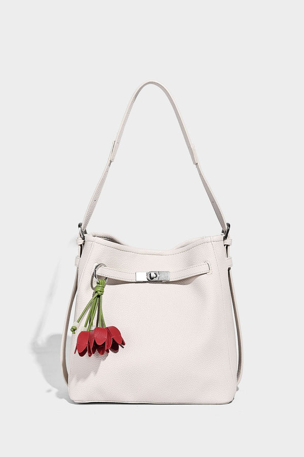 Soft-structured pebbled bucket shoulder bag with front turn-lock strap detail, adjustable strap, and hanging floral tassel
