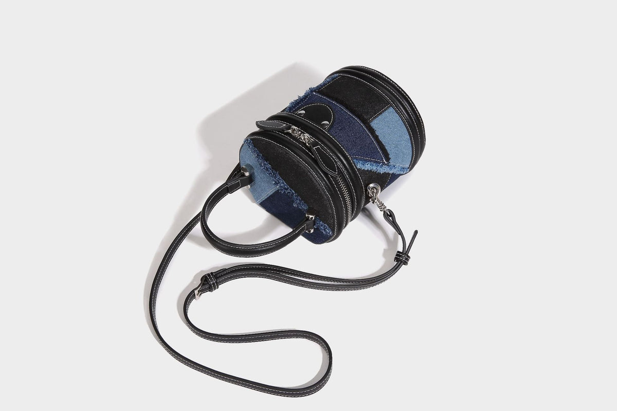 Mini cylindrical barrel bucket bag in denim patchwork with frayed edges, smooth leather-look trim, zip-around top closure