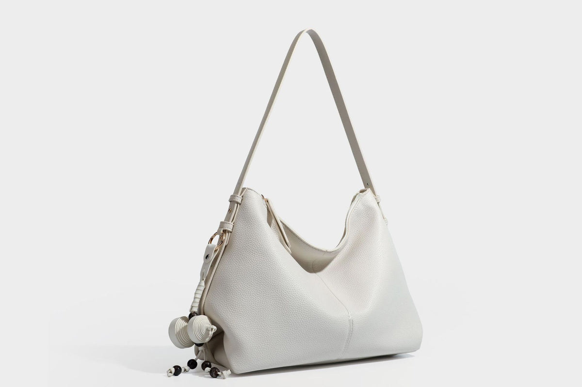 Slouchy hobo shoulder bag with pebbled leather-look finish, zip-top closure, gold-tone hardware, and hanging bead charm
