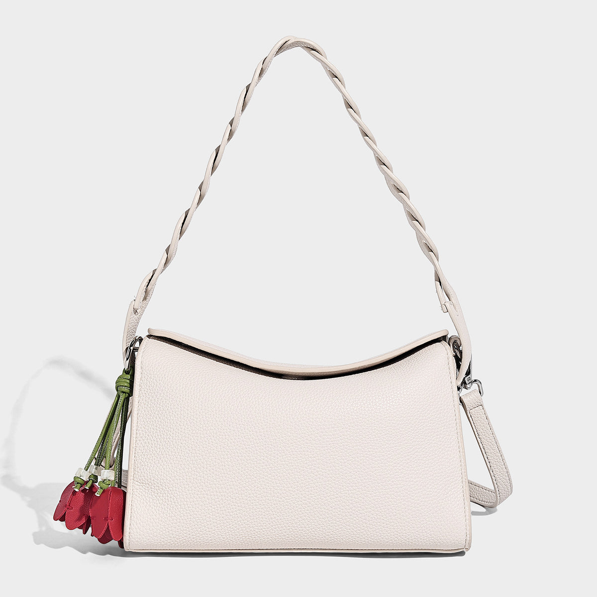 Small structured pebbled-finish shoulder bag with braided top handle, detachable crossbody strap, floral tassel charm, and