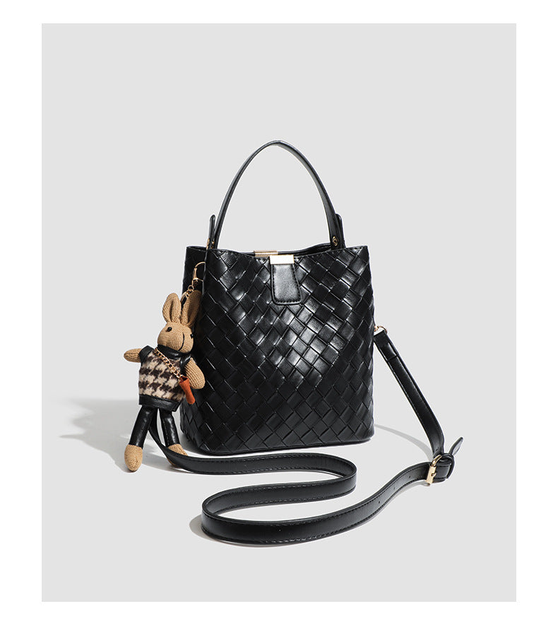 Black woven leather-look bucket bag with gold-tone clip closure, top handle, detachable shoulder strap, and knit bunny charm