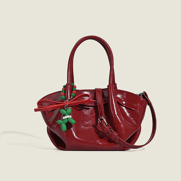 Small structured red glossy PU handbag with bow-and-bead charm, dual top handles, and detachable crossbody strap, front view