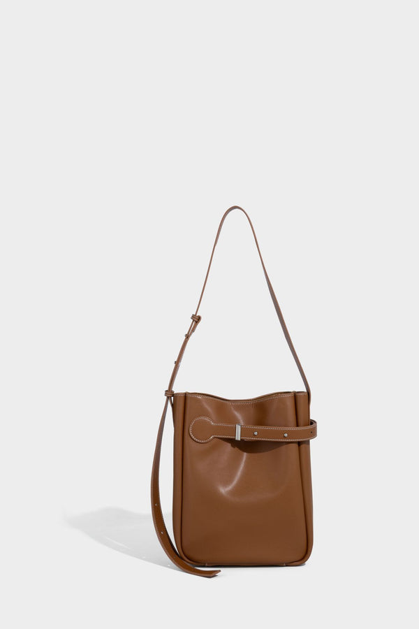 Structured dark brown leather-look bucket bag with white contrast stitching, front wraparound belt buckle strap, and long